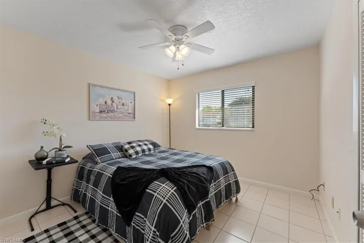 Tiled bedroom with a ceiling fan, baseboards, and a textured ceiling