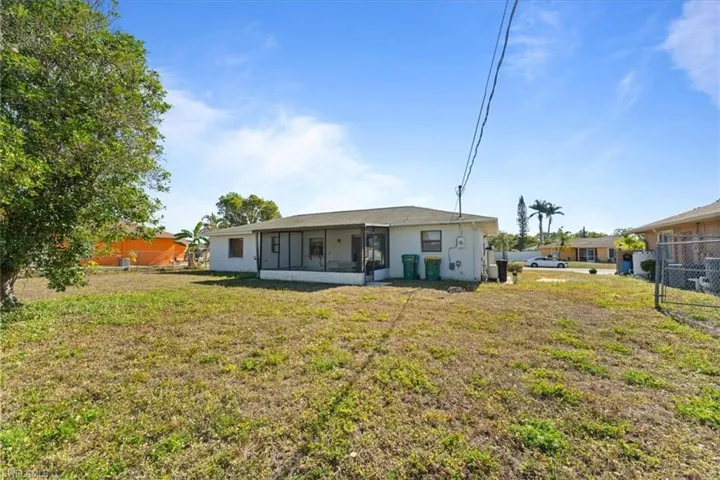 Rear view of property with stucco siding, a sunroom, fence, and a lawn