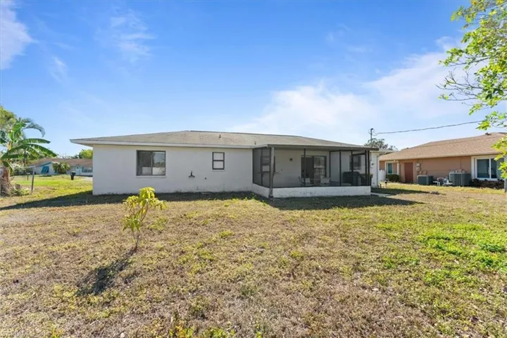Rear view of property with stucco siding, a sunroom, central AC, and a lawn