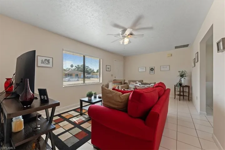 Living room featuring a textured ceiling, light tile patterned flooring, baseboards, visible vents, and ceiling fan