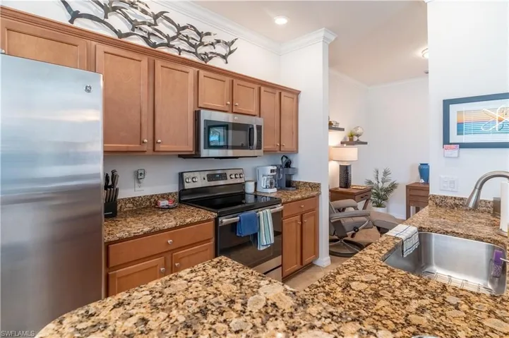 Kitchen with appliances with stainless steel finishes, brown cabinetry, light stone countertops, and crown molding