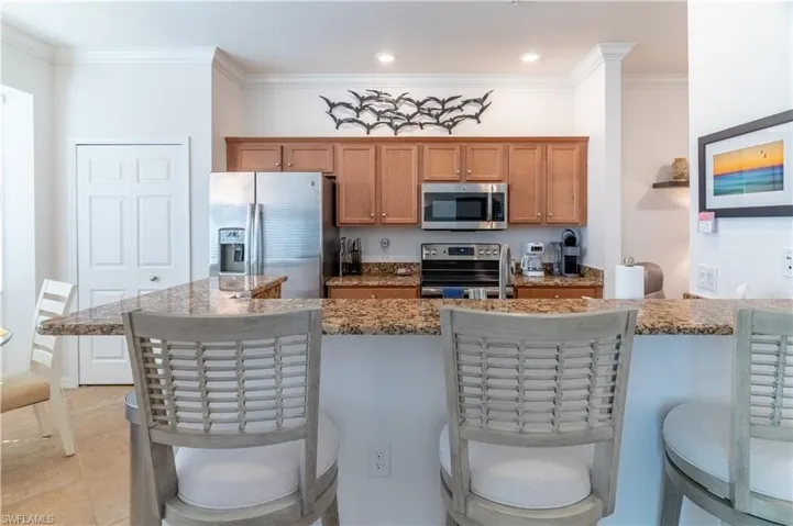 Kitchen with a kitchen bar, appliances with stainless steel finishes, crown molding, light stone countertops, and brown cabinets