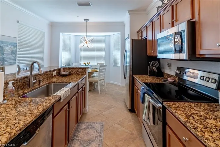 Kitchen featuring stainless steel appliances, brown cabinets, crown molding, dark stone countertops, and pendant lighting