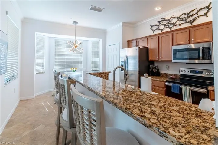 Kitchen with appliances with stainless steel finishes, brown cabinetry, dark stone countertops, a breakfast bar, and ornamental molding