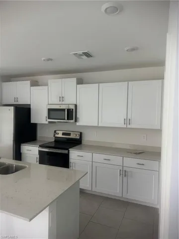 Kitchen featuring white cabinetry, range, light tile patterned floors, and refrigerator