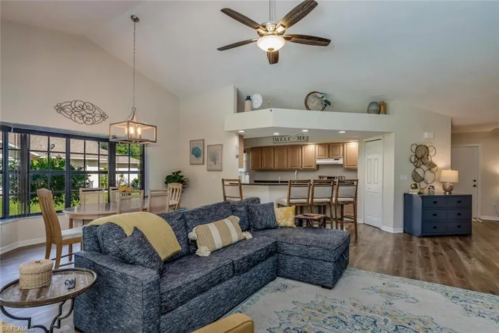 Living room with ceiling fan with notable chandelier, hardwood / wood-style floors, and lofted ceiling
