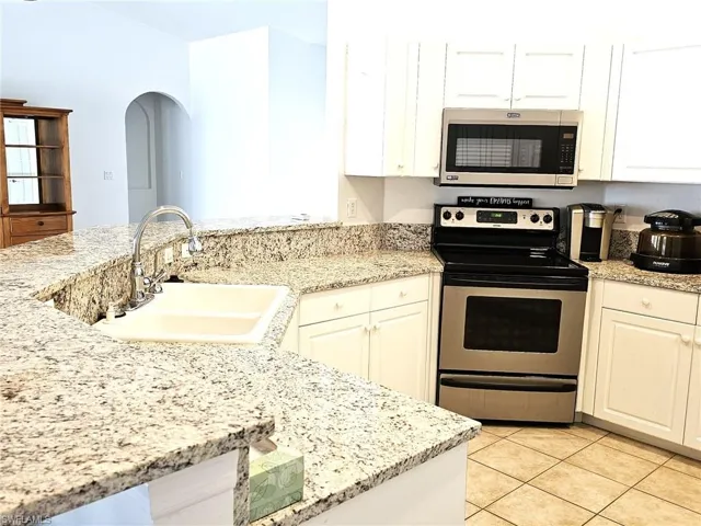 Kitchen with stainless steel appliances, white cabinetry, light stone counters, and light tile patterned floors