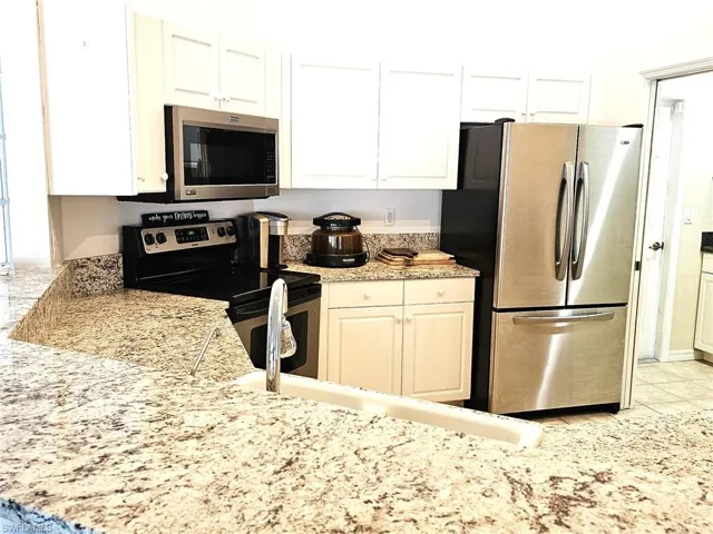 Kitchen featuring stainless steel appliances, white cabinets, light stone counters, and light tile patterned flooring