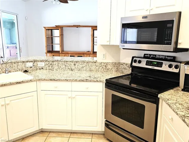 Kitchen with stainless steel appliances, light stone countertops, white cabinets, and a ceiling fan