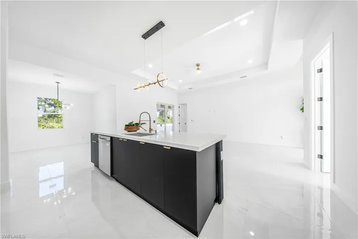 Kitchen with dark cabinets, a tray ceiling, hanging light fixtures, ceiling fan, and a center island with sink