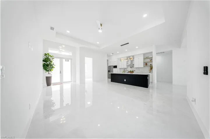 Unfurnished living room featuring a raised ceiling, french doors, a chandelier, recessed lighting, and ceiling fan