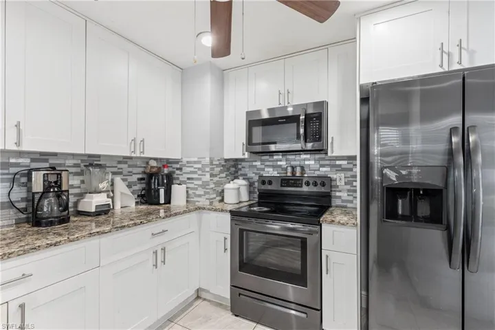 Kitchen featuring white cabinets, light stone counters, ceiling fan, stainless steel appliances, and decorative backsplash