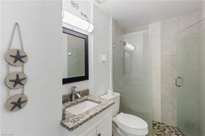 Bathroom featuring a shower with shower door, vanity, and toilet