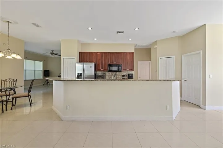 Kitchen featuring light stone counters, stainless steel refrigerator with ice dispenser, a spacious island, black microwave, and ceiling fan