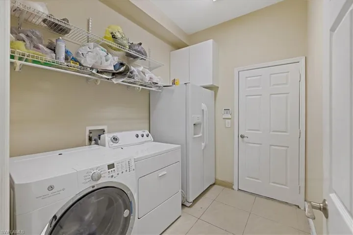 Laundry room with light tile patterned floors, washer and clothes dryer, and cabinet space