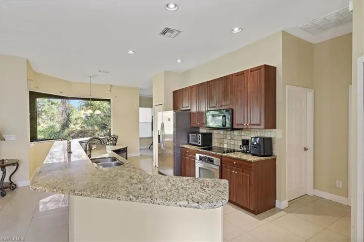 Kitchen with backsplash, light stone countertops, decorative light fixtures, a large island with sink, and black appliances
