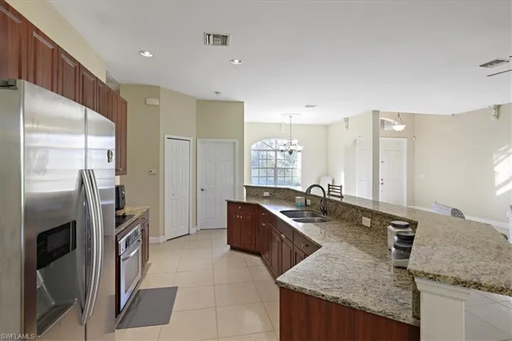 Kitchen featuring stainless steel appliances, light tile patterned flooring, light stone counters, a large island with sink, and recessed lighting