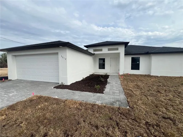 Prairie-style house with stucco siding, an attached garage, and decorative driveway