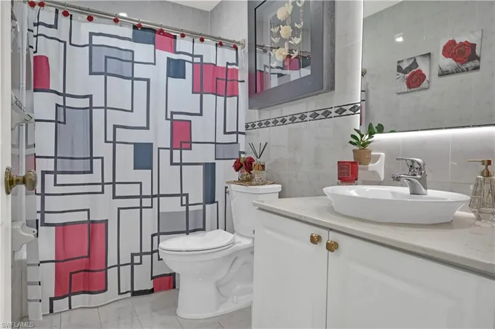 Bathroom with a shower with curtain, toilet, vanity, and tile walls