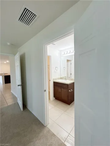 Corridor with light tile patterned floors, visible vents, light carpet, and a sink