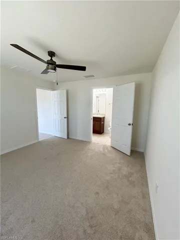 Unfurnished bedroom with visible vents, connected bathroom, baseboards, light carpet, and a ceiling fan