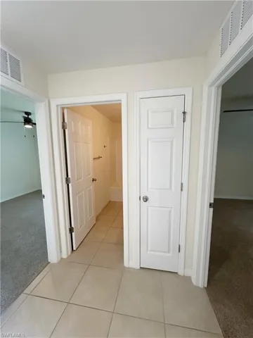 Hall featuring light tile patterned floors, visible vents, light colored carpet, and baseboards