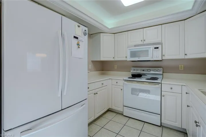 Kitchen featuring white cabinets, light countertops, light tile patterned floors, and white appliances