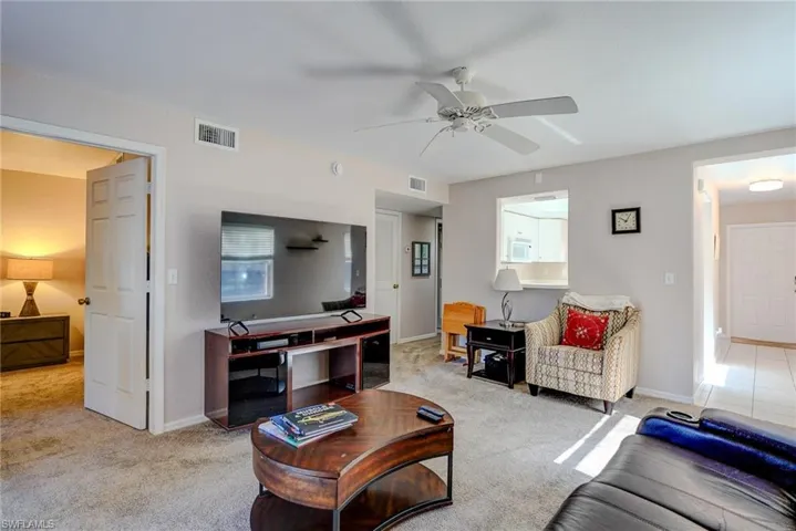 Carpeted living area with visible vents, baseboards, and ceiling fan
