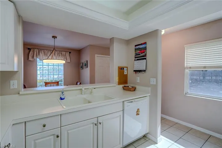 Kitchen featuring white dishwasher, light tile patterned floors, white cabinetry, and a sink
