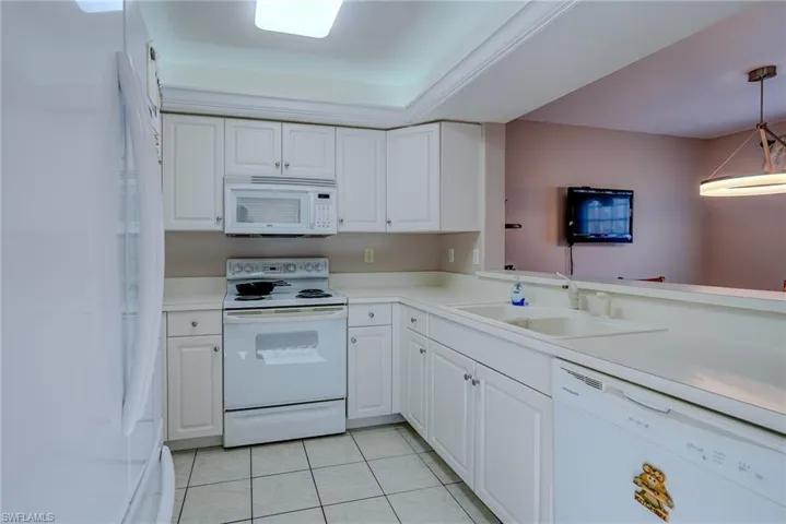 Kitchen featuring white cabinets, light tile patterned floors, a sink, and white appliances