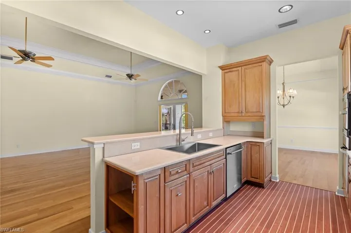 Kitchen featuring wood-finish cabinetry, stainless steel sink with a high-arc faucet, integrated dishwasher, and light-toned countertops
