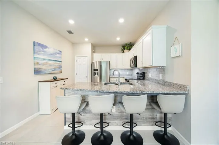Kitchen featuring black appliances, light stone counters, white cabinetry, backsplash, and recessed lighting