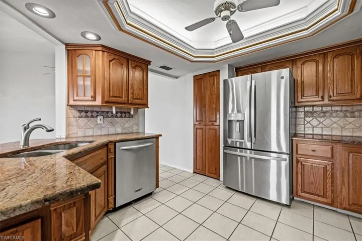 Kitchen with sink, dark stone countertops, a tray ceiling, stainless steel appliances, and crown molding