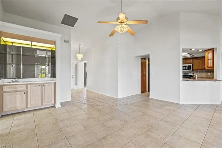 Unfurnished living room featuring high vaulted ceiling, sink, light tile patterned floors, and ceiling fan