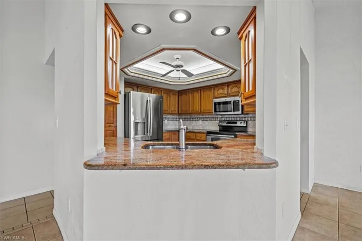 Kitchen with sink, light tile patterned flooring, a raised ceiling, and appliances with stainless steel finishes