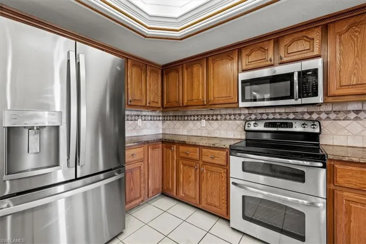 Kitchen with crown molding, appliances with stainless steel finishes, light tile patterned floors, and light stone counters
