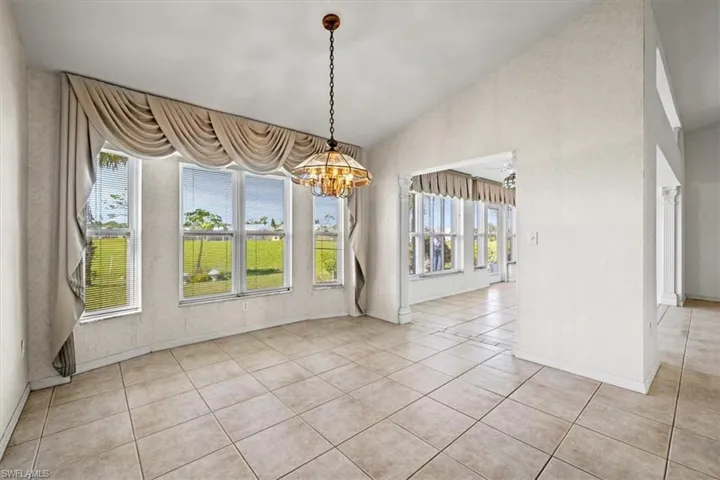 Unfurnished dining area with an inviting chandelier, a water view, lofted ceiling, and light tile patterned floors