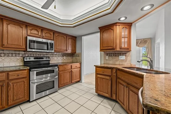 Kitchen featuring sink, light tile patterned floors, appliances with stainless steel finishes, a tray ceiling, and ornamental molding