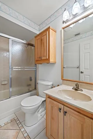 Full bathroom featuring vanity, combined bath / shower with glass door, tile patterned floors, and toilet
