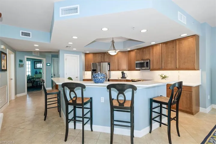 Kitchen featuring wood finish cabinets, a breakfast bar, light countertops, light tile patterned floors, and a tray ceiling