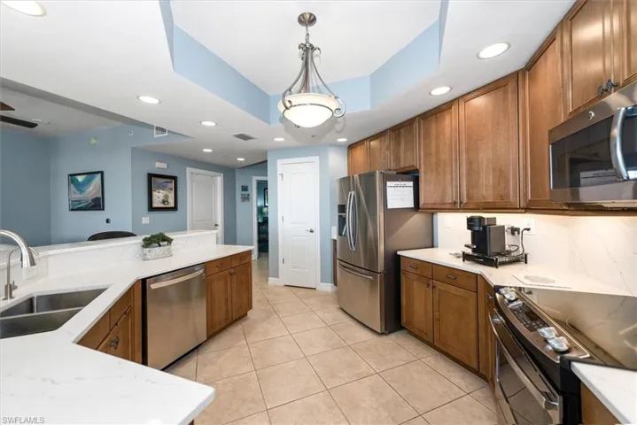 Kitchen featuring stainless steel appliances, wood finish cabinets, decorative light fixtures, light stone countertops, and a tray ceiling