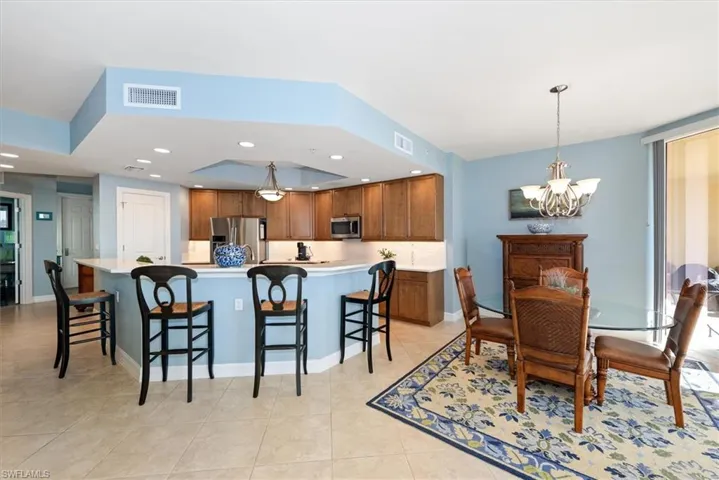 Kitchen with light countertops, a breakfast bar, wood finish cabinetry, stainless steel appliances, and a large island with sink