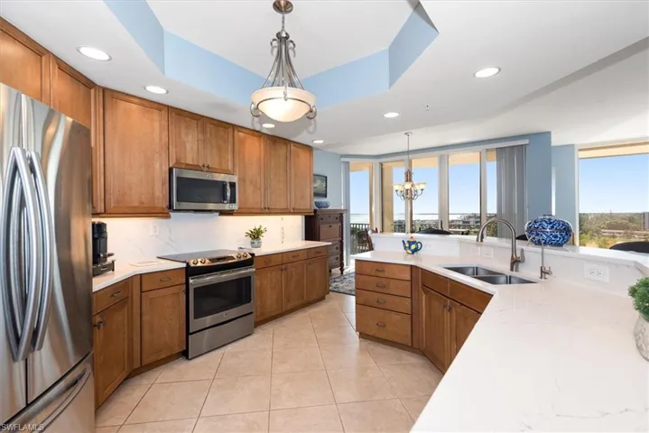 Kitchen with wood finish cabinets, stainless steel appliances, a raised ceiling, decorative backsplash, and light tile patterned floors