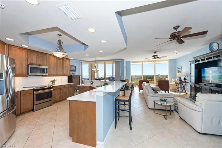 Kitchen with stainless steel appliances, wood finish cabinetry, a breakfast bar area, an island with sink, and a tray ceiling