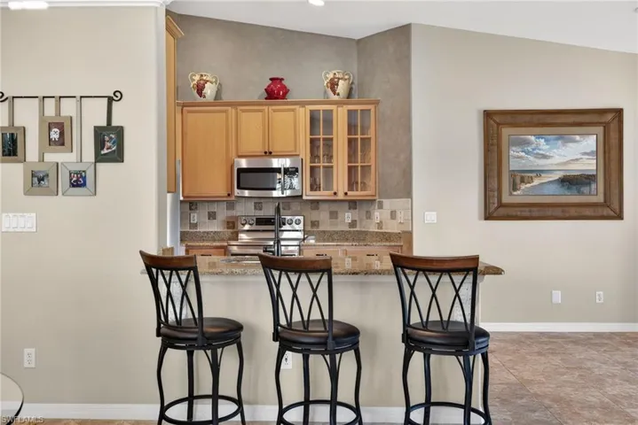 Kitchen with tasteful backsplash, light stone counters, appliances with stainless steel finishes, glass insert cabinets, and a breakfast bar