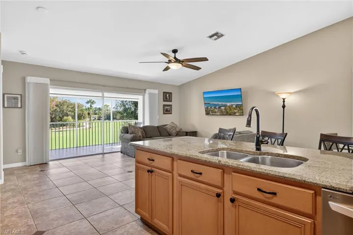Kitchen with light brown cabinetry, open floor plan, light stone counters, dishwasher, and vaulted ceiling
