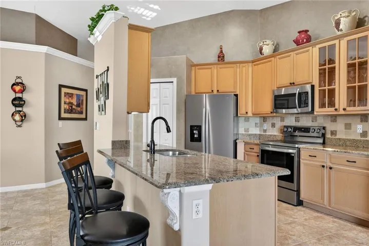 Kitchen with stainless steel appliances, light stone counters, a breakfast bar, and light brown cabinets