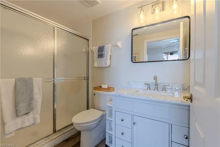 Bathroom featuring toilet, wood finished floors, vanity, visible vents, and a shower stall