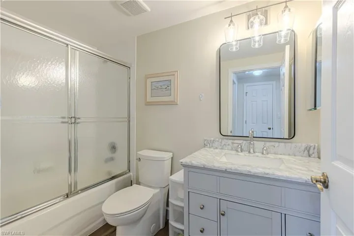 Bathroom featuring vanity, toilet, shower / bath combination with glass door, and visible vents