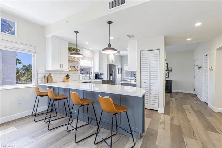 Kitchen with a peninsula, white cabinetry, a kitchen bar, stainless steel fridge, and light countertops